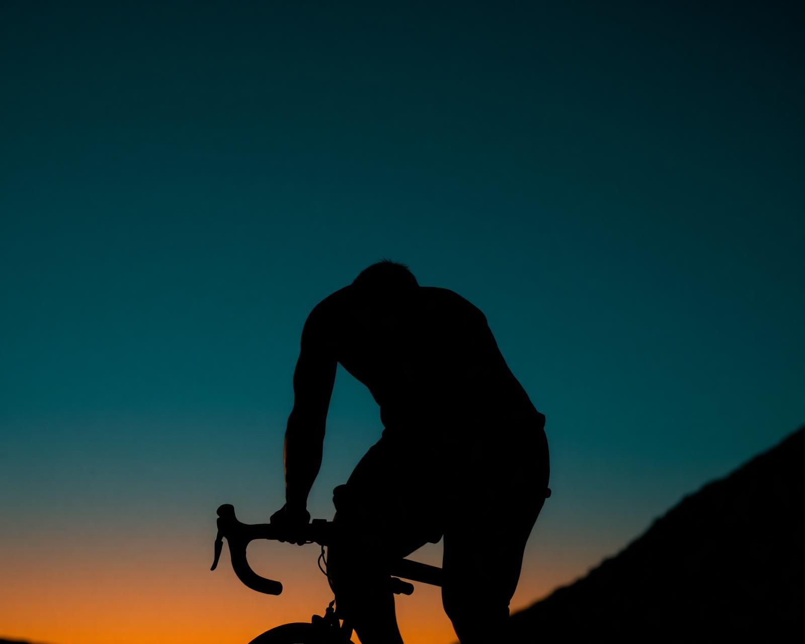 Cyclist climbing at dawn, silhouetted against a teal-and-ember sky